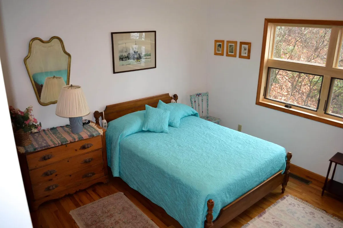 This image features a bedroom with turquoise bedding, a wooden dresser, a decorative lamp, framed artwork, and a window letting in natural light. The setting feels cozy and tranquil, emphasizing the restful atmosphere described in the section.