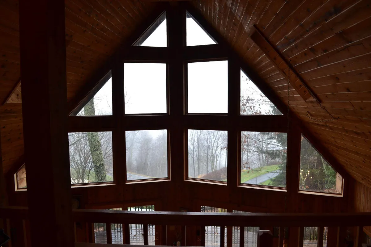 A serene interior scene showcasing large triangular windows that allow abundant natural light to pour into the space. The wooden beams and soft furnishings create a peaceful atmosphere for family gatherings, reading, and admiring the surrounding mountain landscape.