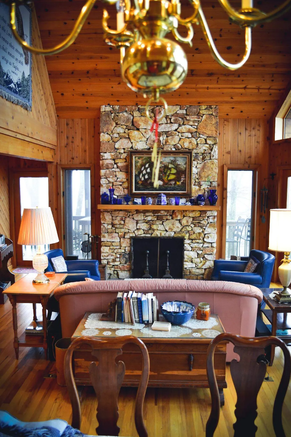 A cozy interior living room with a rustic stone fireplace, wooden furniture, and blue upholstered seating. The space radiates warmth, suggesting evenings spent sharing stories or relaxing after outdoor adventures.