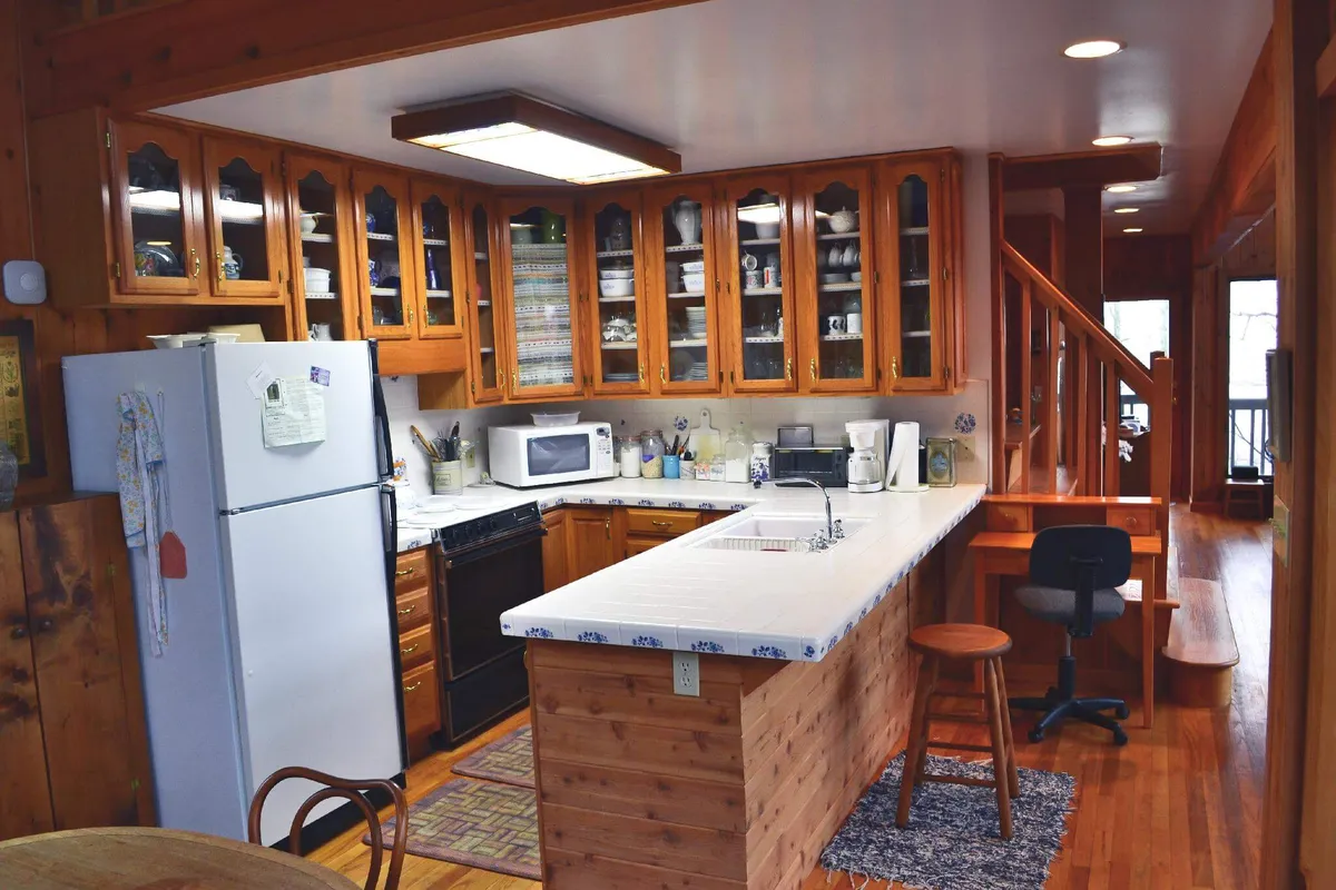 This image features a warm, inviting kitchen with a prominent kitchen island, wooden cabinets, stainless steel appliances, and an adjacent dining table. The setup is open and communal, ideal for group meal preparation or casual conversations while cooking.