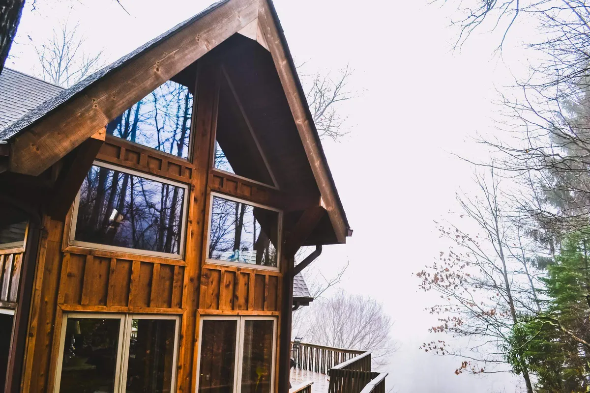 A striking view of the exterior deck area, featuring wooden architectural elements and large windows overlooking a foggy mountain landscape. The deck appears inviting for morning coffee or quiet reflection, with the tranquil mountain air visible in the soft fog and sunrise light.