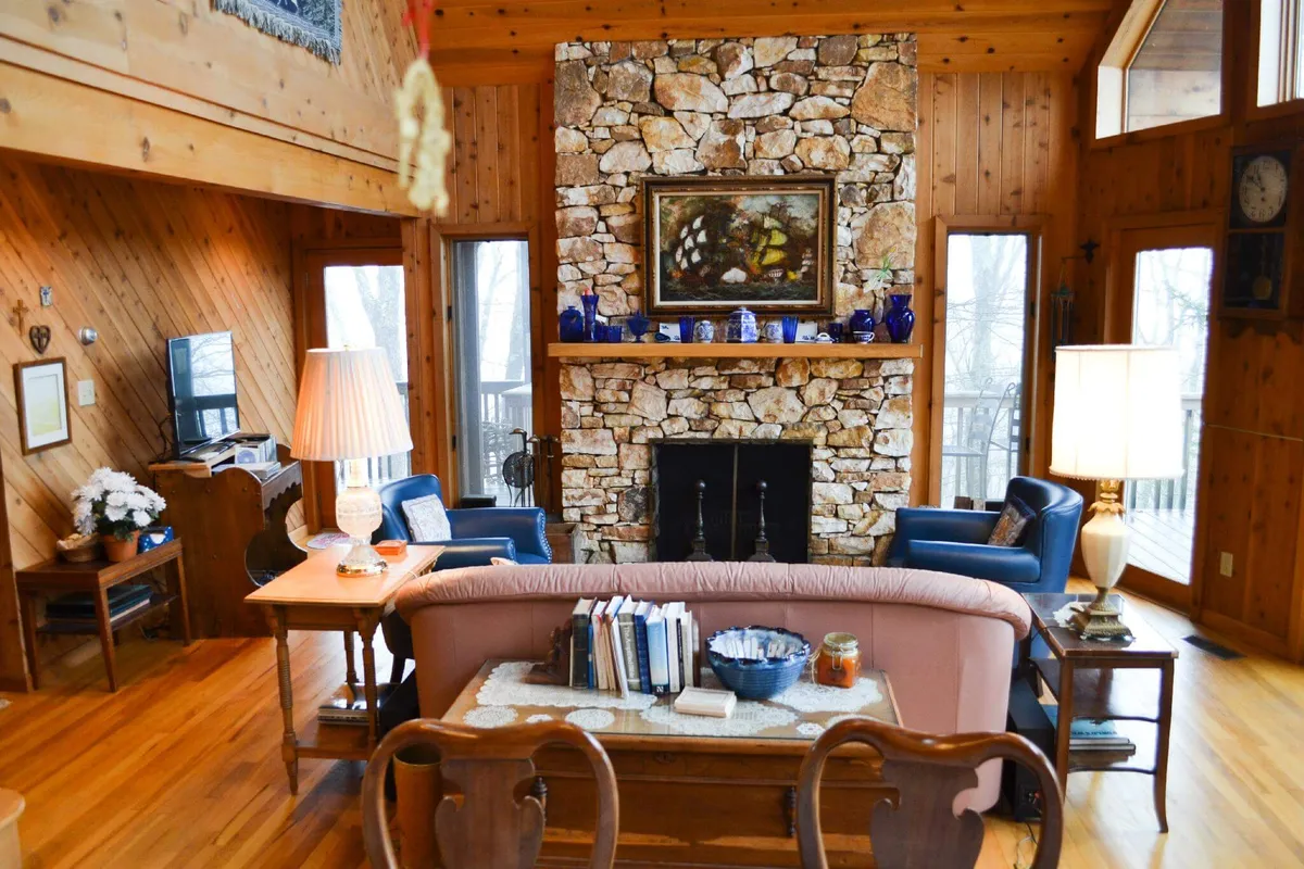 A cozy corner of the living area with a robust stone fireplace as its focal point. Plush blue chairs, a wooden table, and tasteful artwork contribute to a welcoming, intimate environment ideal for reading, socializing, or enjoying a warm drink by the fire.